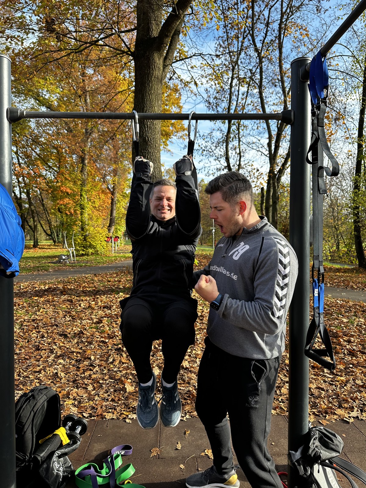 Personal Training outdoor – Coach feuert Klient beim Klimmzug an